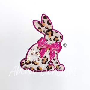 May include: A pink and brown sequined bunny with a pink bow. The bunny is sitting on a white background.