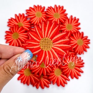 May include: A pile of 15 orange and red embroidered flower patches. The patches are about 2 inches in diameter and have a yellow center.