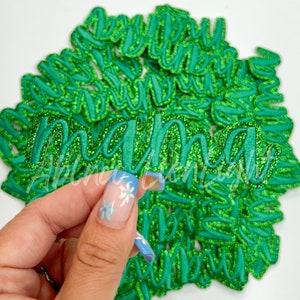May include: A pile of green glitter iron-on patches that spell out "mama".