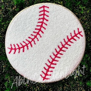 May include: White baseball with red stitching, embroidered on a round white fabric base with a gold glitter trim.