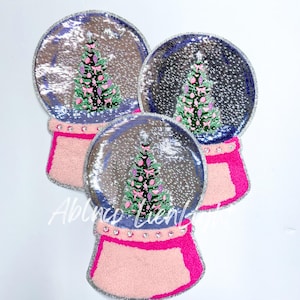 May include: Three silver sequin snow globe patches with pink and green Christmas trees inside. The snow globes have a pink fuzzy base with silver glitter and pink rhinestones.