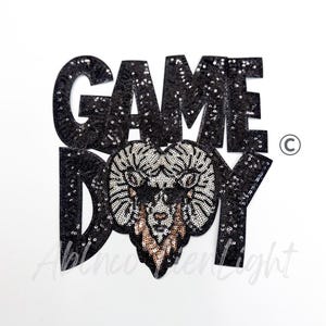 May include: Black sequined patch with the words "GAME DAY" in large block letters. The letter shapes are filled with black sequins. A ram's head design with silver and gold sequins is in the center.
