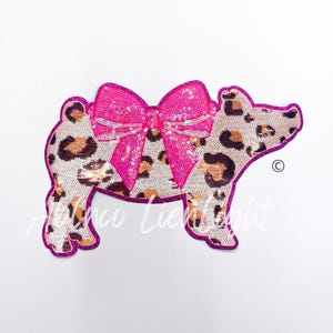 May include: A pink sequined bow on a brown and white leopard print pig applique.