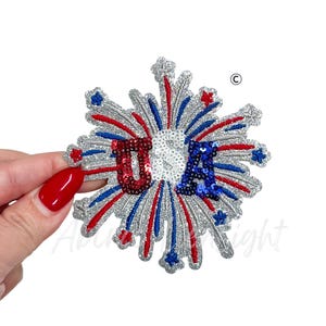 May include: A sparkling, starburst-shaped patch with the letters "USA" in red, white, and blue sequins. The patch features silver glitter accents and red and blue rays, perfect for patriotic crafts and apparel.