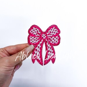 May include: A pink and white glittery bow with a checkered pattern. The bow is made of fabric and has a shiny finish.