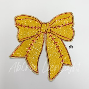 May include: A yellow sequined bow with red stitching, resembling a baseball. The bow is outlined in gold.