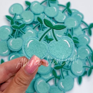 May include: A pile of teal blue embroidered cherry patches. The cherries have green stems and leaves.