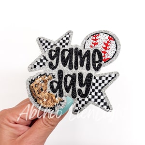 May include: A silver glitter iron-on patch with a black and white checkered star, a baseball, and the text "game day".