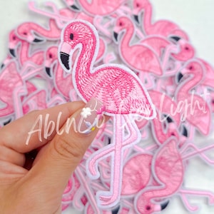 May include: Embroidered pink flamingo patch with a white border. The flamingo has a black beak and is set against a background of other flamingo patches. The patch is approximately 3 inches tall.