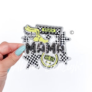 May include: A silver and black sequined iron-on patch with the word "MAMA" in large letters. The patch also features a checkered flag, a stopwatch, and a winged foot.
