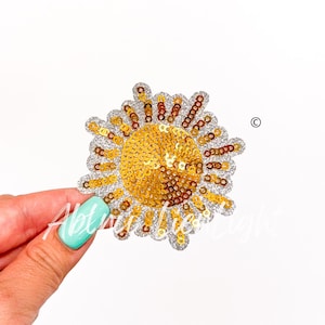 May include: A gold and silver sequin sun applique. The sun is made of gold sequins and has a silver sequin outline. The sun is about 3 inches in diameter.