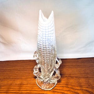 May include: A clear glass vase with a corn-on-the-cob design. The vase has a textured surface with a white interior and a flared top. The base has a decorative, wavy design. The vase is approximately 10 inches tall.