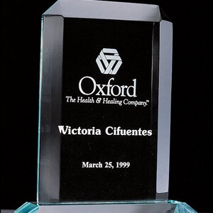 May include: A clear glass award with beveled edges. The award features a white logo for Oxford, The Health & Healing Company, and the text "Victoria Cifuentes" and "March 25, 1999".