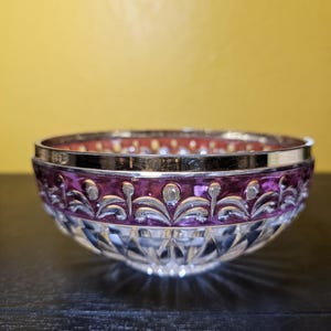 May include: A clear glass bowl with a cut crystal design and a purple rim. The bowl has a silver band around the top.