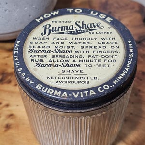 Peut inclure: Un pot en verre vintage avec une texture nervurée et un couvercle en métal foncé portant le texte Burma-Shave. Le couvercle comprend des instructions d'utilisation et indique un contenu net de 1 lb. avoirdupois, fabriqué aux États-Unis.