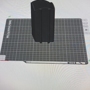 May include: A black, rectangular object with a curved top and vertical grooves. The object is positioned on a gray grid surface, with the text "Bambu Textured PEI Plate" visible. The object appears to be a 3D-printed item.