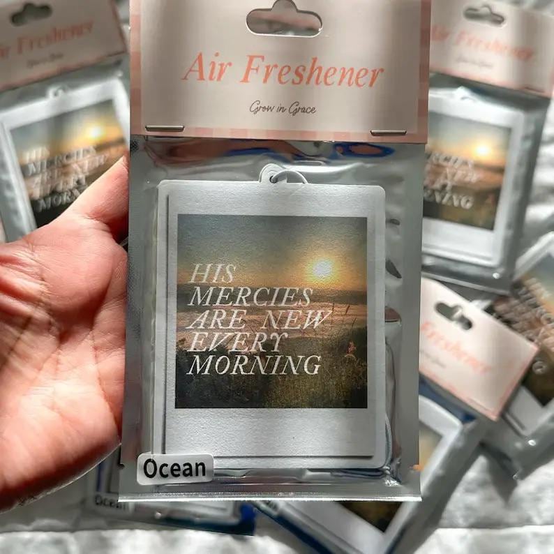 May include: A white car air freshener with a blue ocean scene and the text "His Mercies Are New Every Morning". The air freshener has a label that says "Ocean".