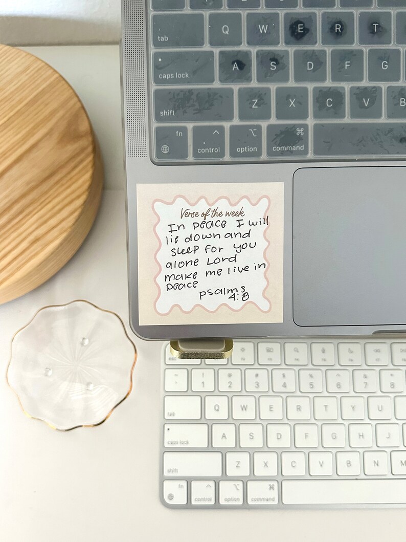 May include: A pink sticky note with rounded corners and a decorative border on a laptop keyboard. The note has the text "Verse of the week" at the top and the following text below: "In peace I will lie down and sleep for you alone Lord make me live in peace Psalms 4:8"