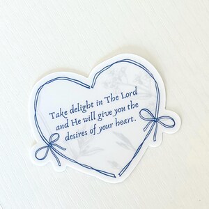 May include: A white heart-shaped sticker with a blue outline and a floral pattern. The sticker has the text "Take delight in The Lord and He will give you the desires of your heart."
