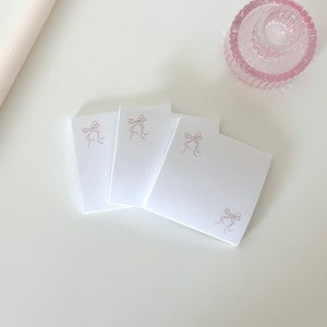Peut inclure: Trois notes adh&eacute;sives carr&eacute;es blanches avec un motif de n&oelig;ud rose sur chaque note.