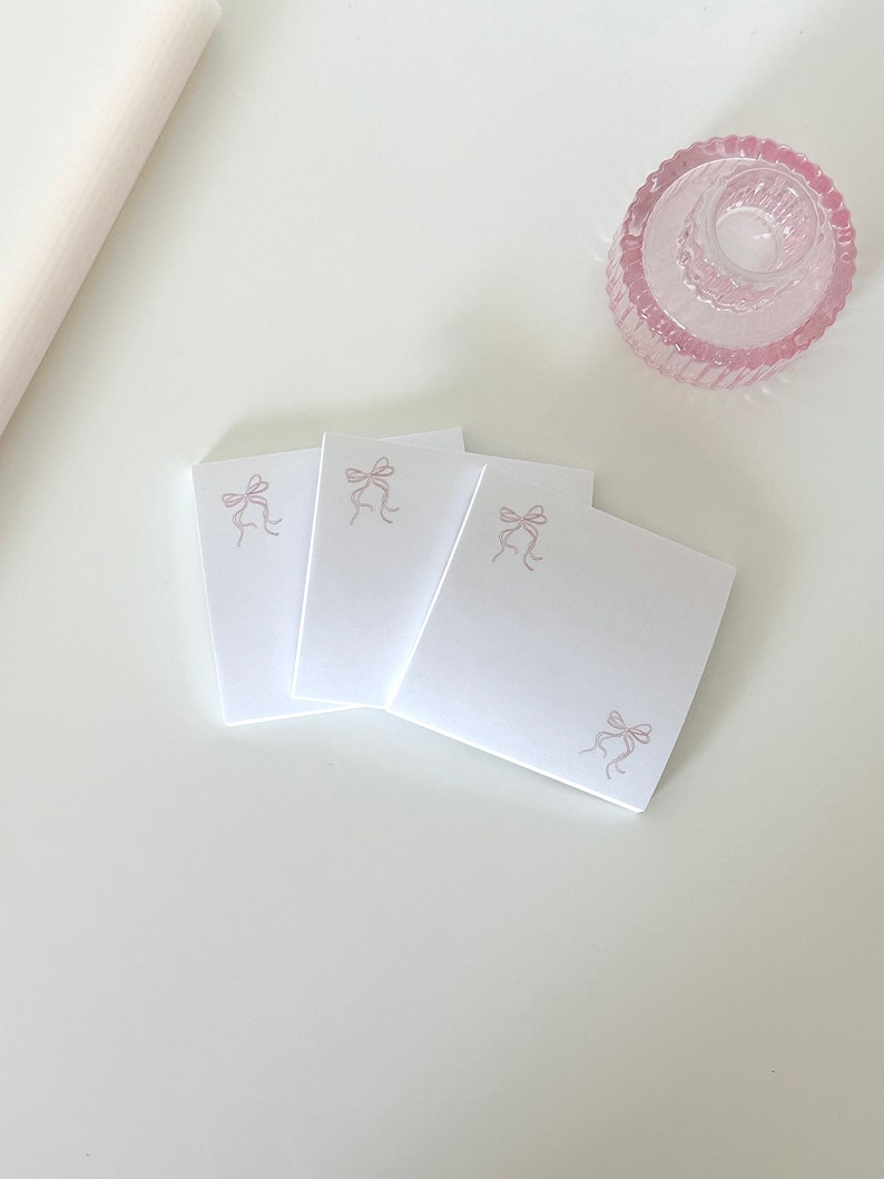 Peut inclure: Trois notes adh&eacute;sives carr&eacute;es blanches avec un motif de n&oelig;ud rose sur chaque note.