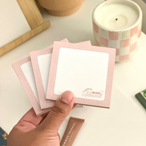 May include: Three pink sticky note pads with a grid pattern and a white writing surface. The top pad has the text "Thankful Grateful Blessed" in red and white.