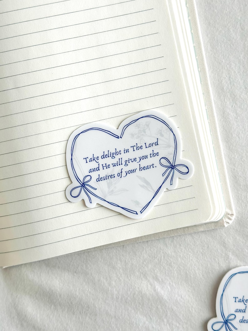 May include: A white heart-shaped sticker with a blue outline and blue ribbon accents. The sticker has a marble-like background and features the text "Take delight in The Lord and He will give you the desires of your heart."