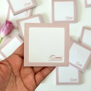 May include: A stack of pink square sticky notes with a grid pattern and the text "Thankful Grateful Blessed" on one note.