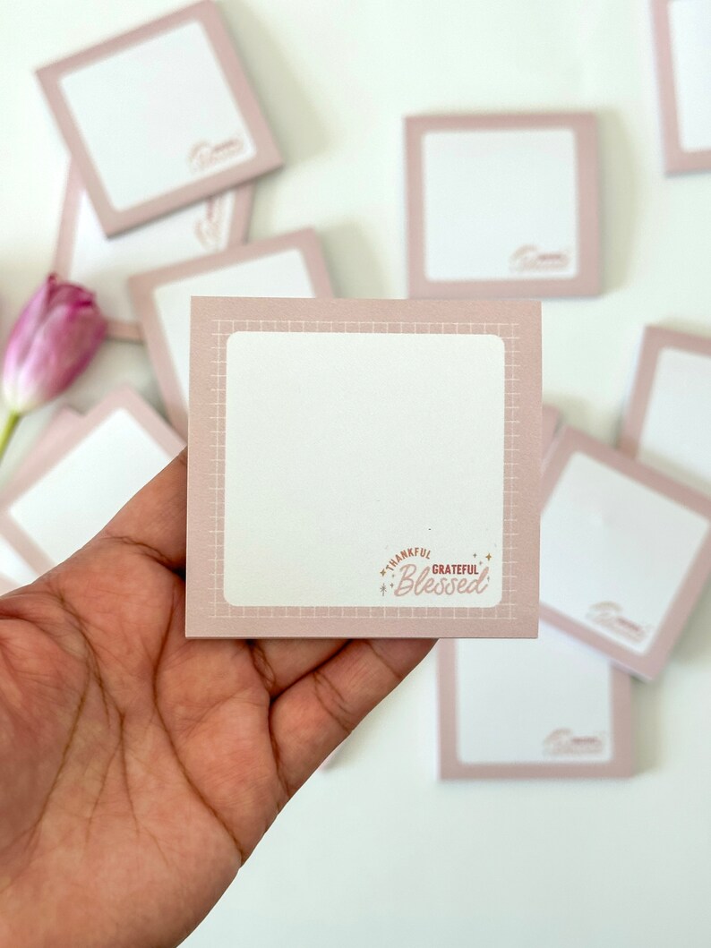 May include: A stack of pink square sticky notes with a grid pattern and the text "Thankful Grateful Blessed" on one note.