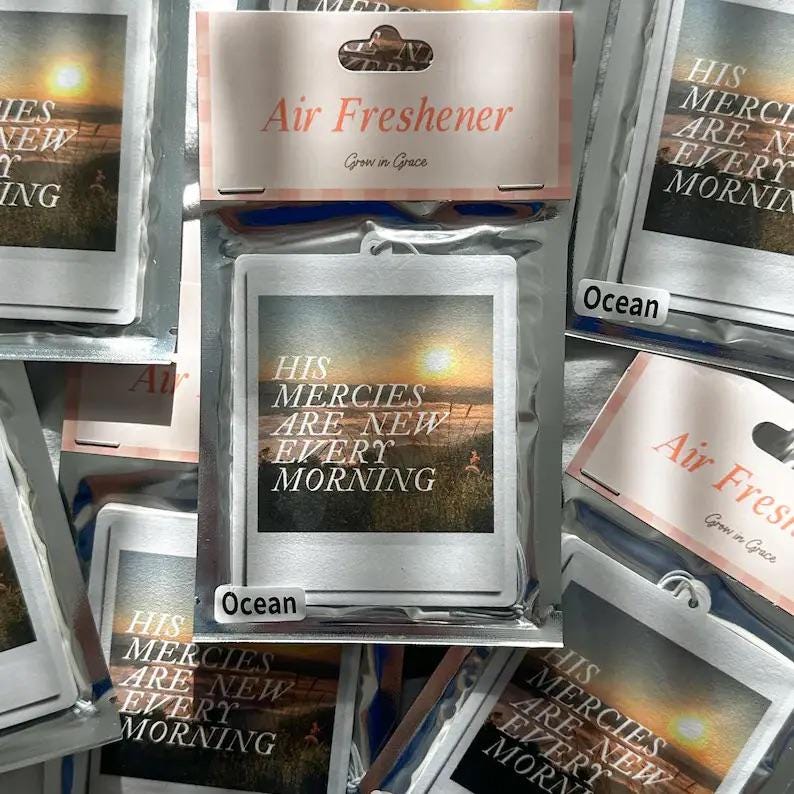May include: A white car air freshener with a sunset scene and the text "His Mercies Are New Every Morning" in a pink and white font. The air freshener is labeled "Ocean" and "Grow in Grace".