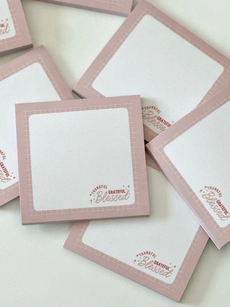 May include: A stack of pink sticky notes with a white square in the centre and the text "Thankful Grateful Blessed" in a pink and red font.