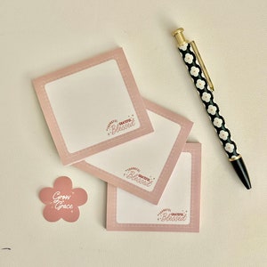 May include: Three pink square sticky notes with the text "Thankful Grateful Blessed" in a white circle with stars. A pink flower sticker with the text "Grow Grace" and a black and white pen with a floral pattern.