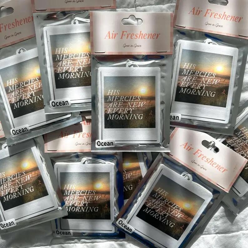 May include: A close-up of several car air fresheners with a sunset scene and the text "His mercies are new every morning". The air fresheners are packaged in clear plastic bags with a white header that says "Air Freshener".