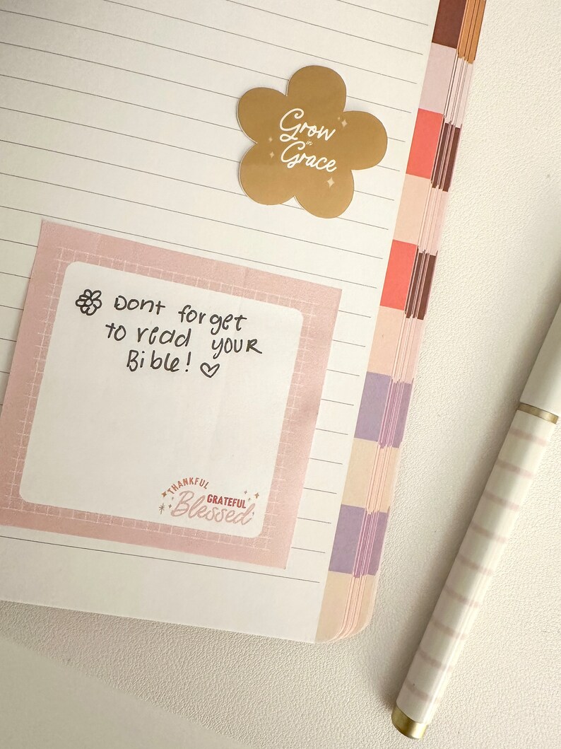 May include: A pink sticky note with the text "Don't forget to read your Bible!" and a small flower graphic. The note is on a lined notebook page with a gold flower sticker that says "Grow in Grace".