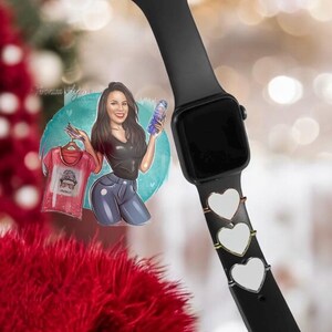 Op de afbeelding: Een zwarte Apple Watch met een zwarte band en drie zilveren hartvormige bedels. Het horloge is op een witte achtergrond.