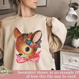 May include: A beige sweatshirt with a vintage-style illustration of a deer wearing a wreath of Christmas ornaments and a pink bow.