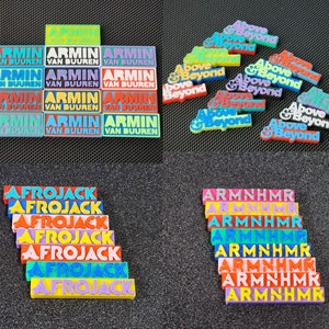 May include: A collection of colorful, rectangular, plastic name tags with the names "Armin van Buuren", "Above & Beyond", "Afrojack", and "Armnhmr" printed on them.