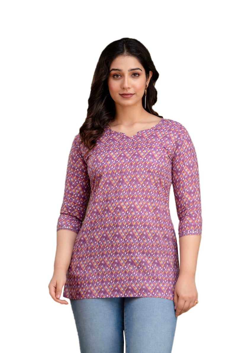 Puede incluir: Una blusa morada con un estampado geom&eacute;trico. La blusa tiene cuello en V y mangas tres cuartos. La tela presenta un patr&oacute;n repetido de diamantes en tonos morados, amarillos y blancos. La blusa se combina con vaqueros azules.