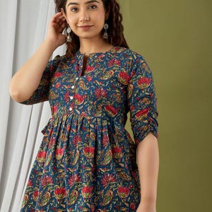 Puede incluir: Top azul con estampado floral, cuello mandar&iacute;n y mangas tres cuartos. El top presenta una cintura fruncida y una botonadura frontal. El estampado floral incluye flores rojas y amarillas.
