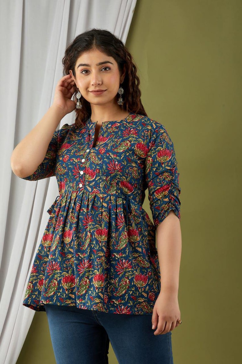 Puede incluir: Top azul con estampado floral, cuello mandar&iacute;n y mangas tres cuartos. El top presenta una cintura fruncida y una botonadura frontal. El estampado floral incluye flores rojas y amarillas.