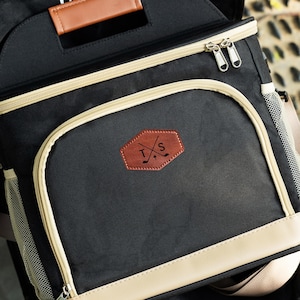May include: Black and beige insulated cooler bag with a brown leather patch featuring the initials "T.S." and crossed golf clubs.
