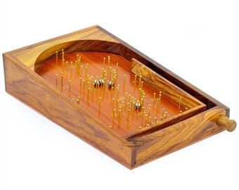 May include: A wooden game with a slanted playing surface and a row of metal pins. The game is designed to launch small metal balls into the holes at the bottom of the playing surface. The game is made of dark wood with a natural finish.