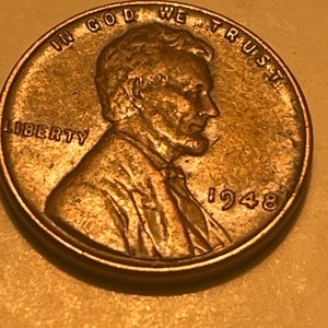 May include: A copper-colored 1948 US penny coin with the profile of Abraham Lincoln on the obverse side. The coin has the words "IN GOD WE TRUST" and "LIBERTY" inscribed around the edge.