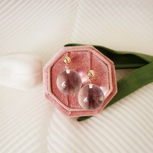 May include: A pair of gold earrings with clear glass orbs. The earrings are displayed in a pink velvet jewelry box.