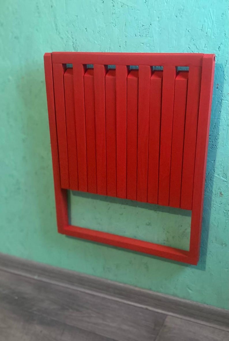 May include: A red folding chair with a slatted back and a simple frame. The chair is folded and mounted on a wall.