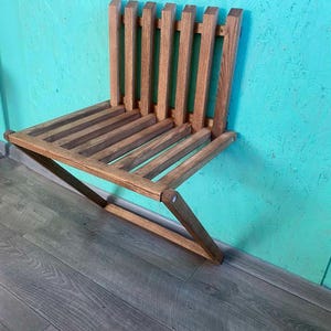 Könnte beinhalten: Ein faltbares Wandregal aus Holz mit hellbrauner Oberfläche. Das Regal besteht aus Latten und hat ein schlichtes, modernes Design.