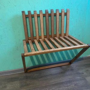 May include: A wooden bench with a slatted design. The bench is made of natural wood and has a rustic look. It is mounted to the wall and has a simple, minimalist design.