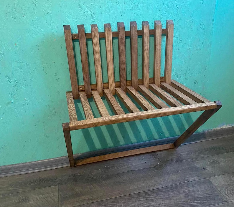 May include: A wooden bench with a slatted design. The bench is made of natural wood and has a rustic look. It is mounted to the wall and has a simple, minimalist design.