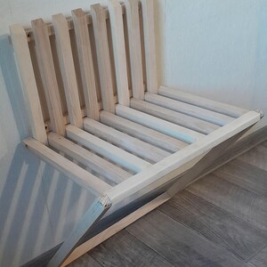 May include: A light wood folding chair with a slatted back and seat. The chair is folded and leaning against a wall.