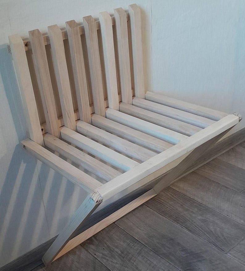 May include: A light wood folding chair with a slatted back and seat. The chair is folded and leaning against a wall.